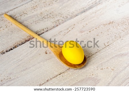 Yellow easter egg in wooden spoon on wooden white shabby background