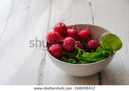Bunch of fresh radishes in white bowl on old white board