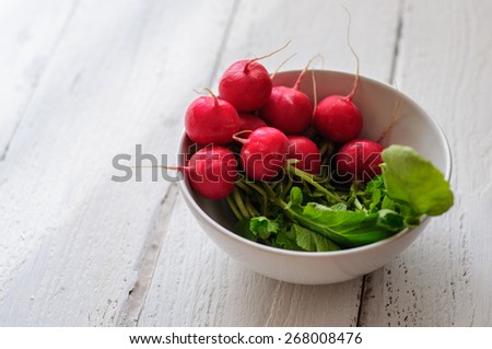 Bunch of fresh radishes in white bowl on old white board