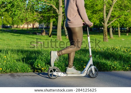 Young woman in sports wear on kick scooter in park