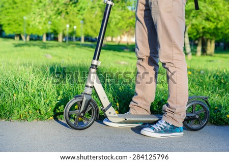 Young man in casual wear on kick scooter in park at sunset
