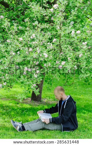 Young man reads a book under blooming apple tree