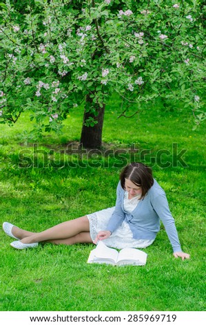 Young woman reads a book under blooming apple tree