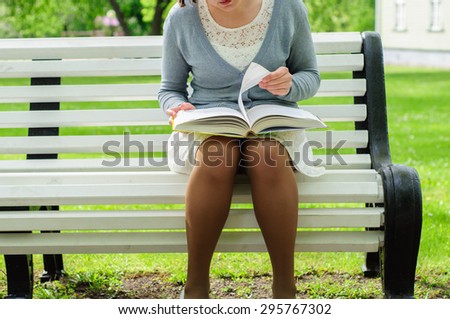 Young woman reads a book with emotions on a bench in park