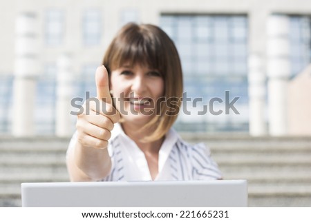 Business woman sitting on the stairs gives thumbs up for business success