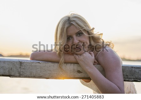 Portrait of beautiful blond curly woman sitting on old wooden bench with lake behind.