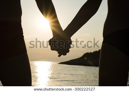 Closeup of a couple holding hands on a beach at sunset, silhouette effect.