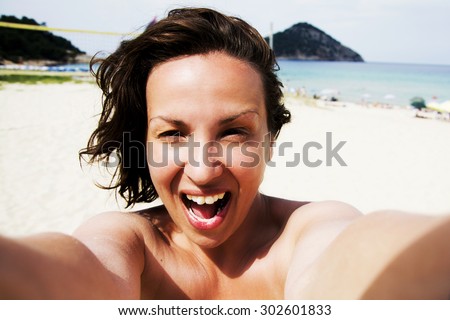 Beautiful young smiling woman making self portrait on a beach, She is excited about vacation and having great time on amazing sandy beach. She is laughing out loud.