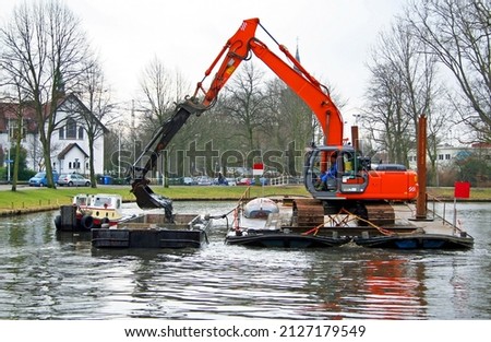 Dredging of urban canals by crane from a pontoon, the dredging spoil is deposited in a barge for transportation  Leiden, Netherlands Imagine de stoc © 