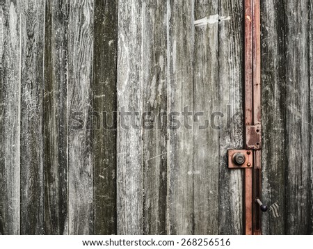 A battered old wooden door with scratched faded vertical panels and a red metal lock, Columbus, Ohio USA. Textured wood grain abstract background with copy space.