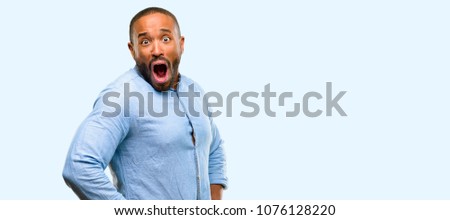 African american man with beard happy and surprised cheering expressing wow gesture isolated over blue background