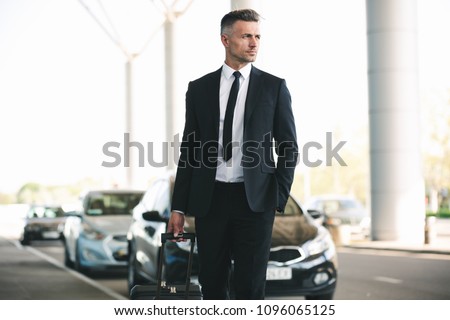 Handsome mature businessman catching a taxi while walking outside the airport with a suitcase
