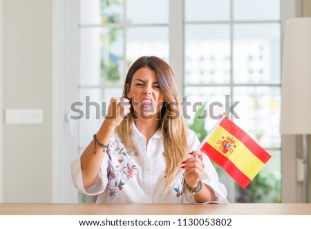 Young woman at home holding flag of Spain annoyed and frustrated shouting with anger, crazy and yelling with raised hand, anger concept