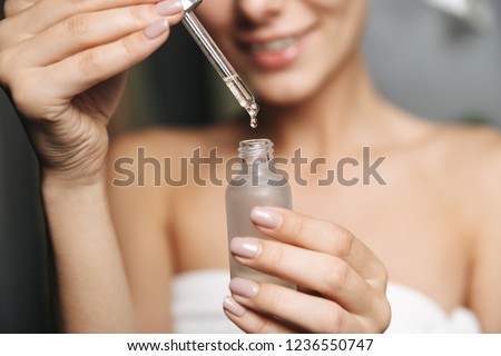 Close up of a beautiful young woman wrapped in towel applying cosmetic oil from a bottle on her face