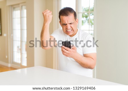 Middle age man using smartphone at home annoyed and frustrated shouting with anger, crazy and yelling with raised hand, anger concept