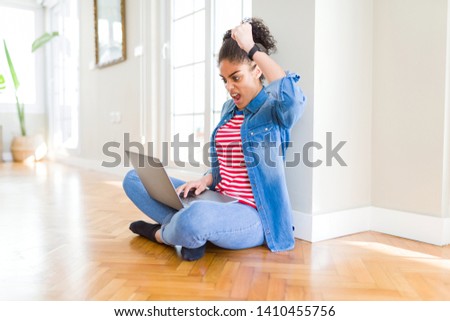Young african american woman sitting on the floor using computer laptop annoyed and frustrated shouting with anger, crazy and yelling with raised hand, anger concept