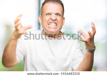 Middle age arab man wearig white t-shirt over isolated background Shouting frustrated with rage, hands trying to strangle, yelling mad