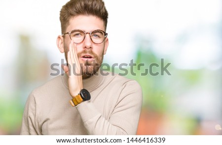 Young handsome business man wearing glasses hand on mouth telling secret rumor, whispering malicious talk conversation