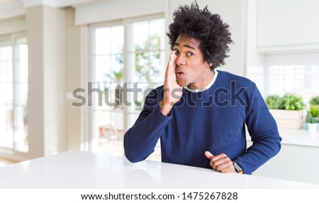 Young african american man wearing casual sweater sitting at home hand on mouth telling secret rumor, whispering malicious talk conversation