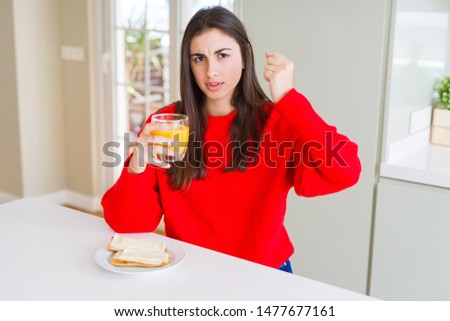 Beautiful young woman eating toasts and orange juice for snack or breakfast annoyed and frustrated shouting with anger, crazy and yelling with raised hand, anger concept