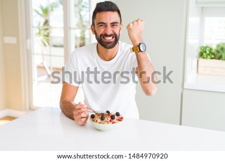 Handsome hispanic man eating healthy breakfast in the morning at home annoyed and frustrated shouting with anger, crazy and yelling with raised hand, anger concept