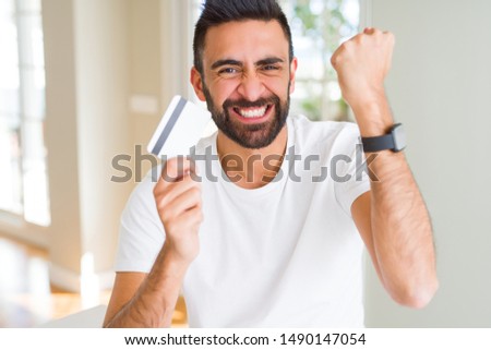 Handsome hispanic man holding credit card annoyed and frustrated shouting with anger, crazy and yelling with raised hand, anger concept