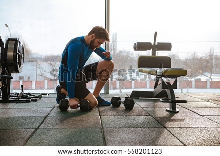 Image of concentrated young sportsman in gym make sport exercises with dumbbells.