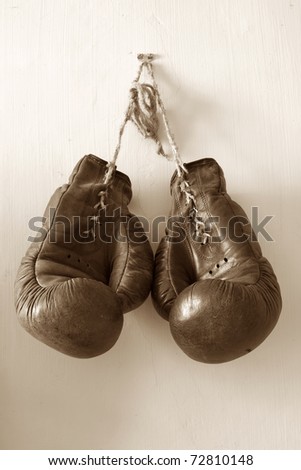 hang up the gloves, old worn leather boxing gloves in sepia tones, hanged up on grunge style wall.