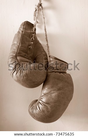 hang up the gloves, old worn leather boxing gloves in sepia tones, hanging on grunge style wall.