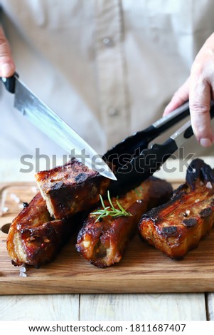 Selective focus. Soft focus. Defocus. Appetizing BBQ ribs. Chef with a knife cuts barbecue ribs on the board.