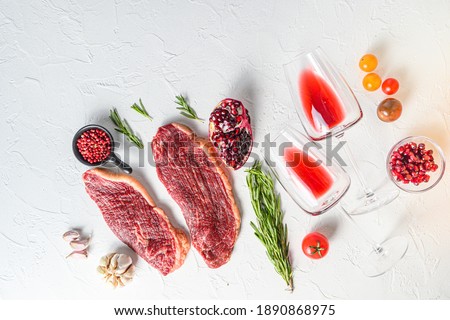 Picanha organic beef steaks with rosemary, peppercorns, pomegranate, near red wine in glasses and bottle over white textured background, top view