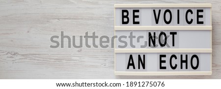 'Be voice not an echo' on a lightbox on a white wooden background, top view. Flat lay, overhead, from above. Copy space.
