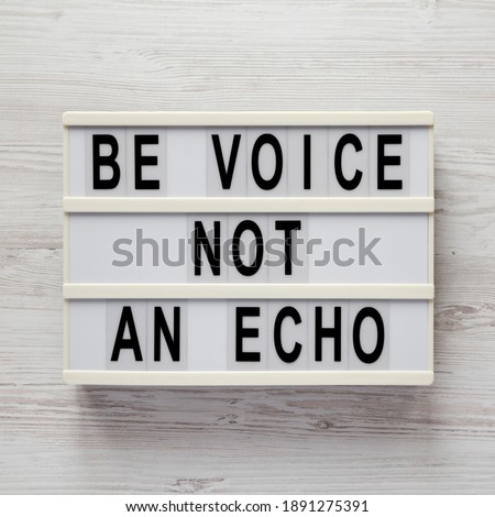 'Be voice not an echo' on a lightbox on a white wooden background, top view. Flat lay, overhead, from above. 