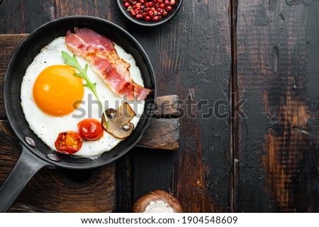 Scrambled eggs in frying pan with pork lard, bread and green feather in cast iron frying pan, on old dark wooden table background, top view flat lay , with space for text copyspace