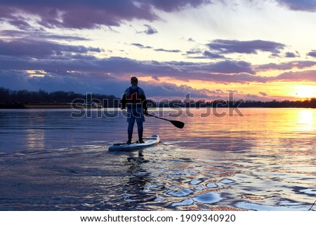 Boy rowing on stand up paddle boarding (SUP) paddling along the calm autumn Danube river against background of a colorful sunset. The concept of children's sports and tourism. Stock fotó © 