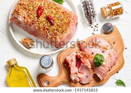 Assorted raw organic meat. Pork fillet and steaks for grilling, baking, or frying. Flakes spices and oil on a white putty background, close up