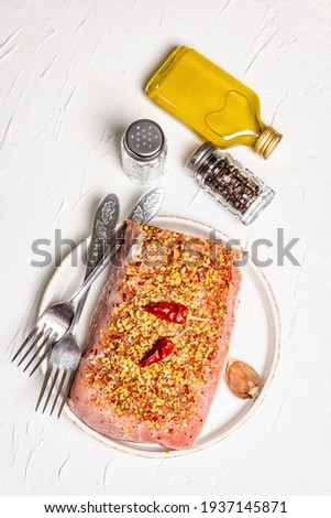 Raw organic meat. Pork fillet for grilling, baking, or frying. Flakes spices, cutlery, oil on a white putty background, top view