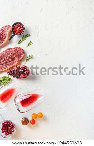 Set of picanha organic beef steaks with rosemary, peppercorns, pomegranate, near red wine in glasses and bottle over white textured background, top view with space for text