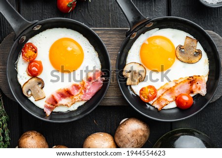 Scrambled eggs in frying pan with pork lard, bread and green feather in cast iron frying pan, on black wooden table background, top view flat lay