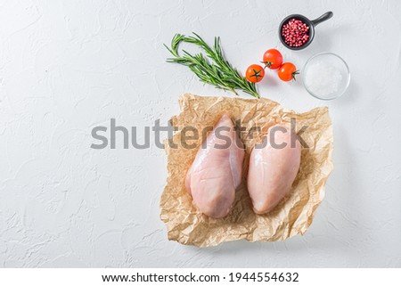 Raw chicken breast oon craft paper over textured white background top view space for text