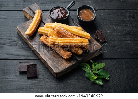 Churros with caramel, Traditional Spanish cusine, on black wooden table background