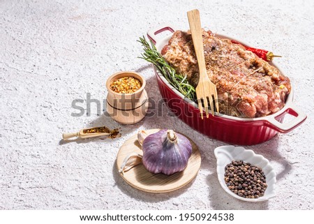 Raw pork roll stuffed with garlic and carrots in a ceramic roasting dish. Fresh meat, spices, rosemary, garlic. Light putty background, modern hard light, dark shadow, copy space