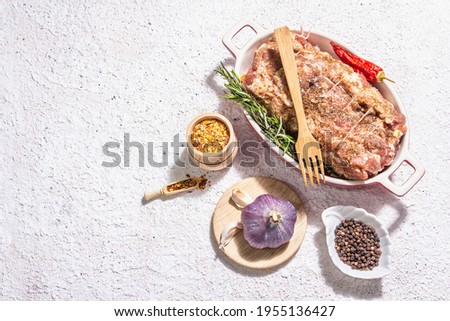 Raw pork roll stuffed with garlic and carrots in a ceramic roasting dish. Fresh meat, spices, rosemary, garlic. Light putty background, modern hard light, dark shadow, top view