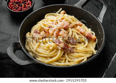 Traditional italian dish spaghetti carbonara with bacon in a cream sauce set, in cast iron frying pan, on black stone background