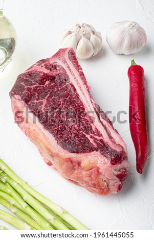 Club raw steak with herbs and salt prepared for cooking, on white stone background