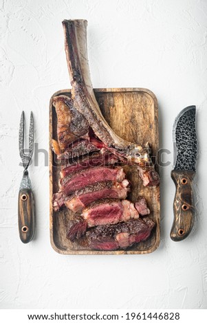 Sliced Tomahawk Steak on the bone set, on wooden serving board, on white stone background, top view flat lay, with copy space for text