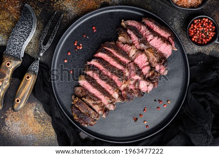 Fresh grilled meat. Grilled beef steak medium rare black angus rib eye steak set, on plate, with meat knife and fork, on old dark rustic background, top view flat lay