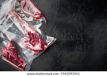 Dry aged steak in a vacuum. Meat products in plastic pack set, tomahawk, t bone and club steak cuts, on black stone background, top view flat lay, with copy space for text