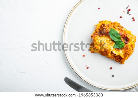 Traditional lasagna made with minced beef bolognese sauce topped with basil leafs set, on plate, on white stone background, top view, flat lay, with copy space for text
