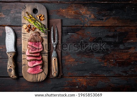 Sliced grilled marbled meat steak Filet Mignon set, with onion and asparagus, on wooden serving board, with meat knife and fork, on old dark wooden table background, top view flat lay, with copy space Сток-фото © 